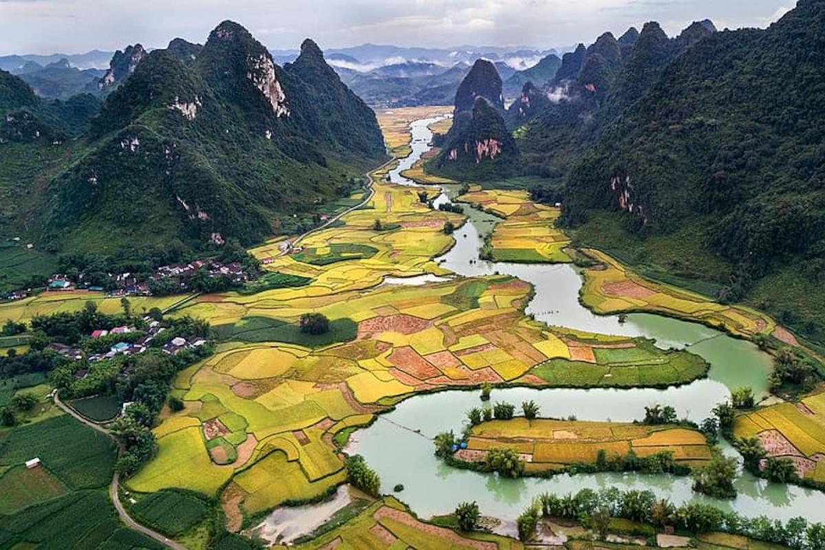 Steep forested towers of rock rise abruptly from a patterned set of small farm fields along a winding river